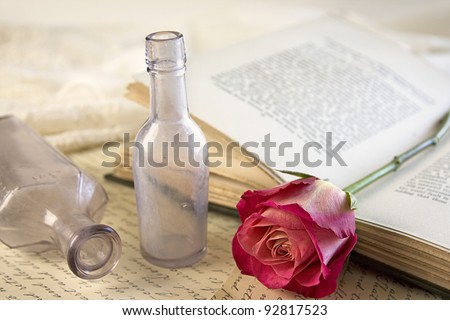 A single red rose laying on top of an opened vintage book with a couple of vintage apothecary bottles.