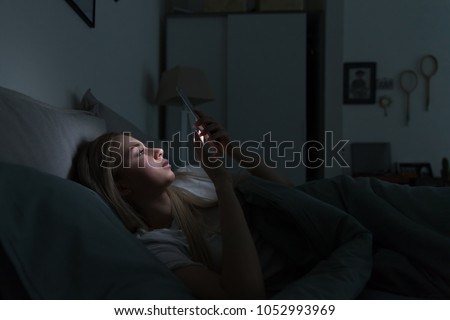 Portrait of young sleepy exhausted woman lying in bed using smartphone at late night, can not sleep/ Insomnia, nomophobia, sleep disorder concept/ Dependency on a cell phone