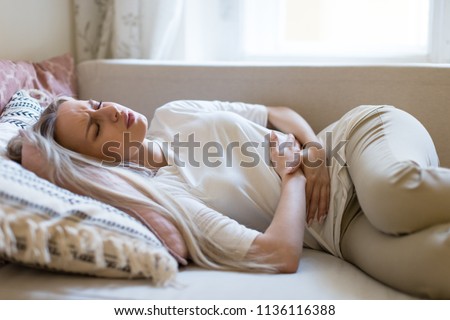 Health issues problems.Young Caucasian woman suffering from stomach pain, feeling abdominal pain or cramps, lying on sofa.Period menstruation, female health problem, aching belly and gynecology