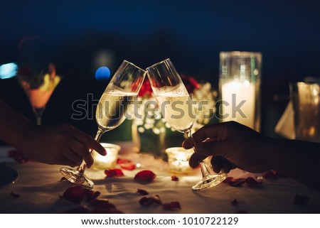 Romantic candlelight dinner table setup. Man & Woman hold glass of Champaign.