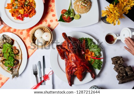 Concept picture for Chinese new year table set up and Chinese dishes. Men and Women are serving tea and crispy duck.