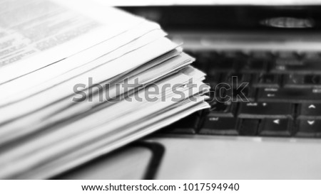 Newspapers and laptop. Pile of daily papers with news on the computer. Pages with headlines, articles folded and stacked on keypad of electronic device. Modern gadget and old journals, focus on paper