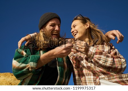 Laughing couple of friends hipsters passing a joint and hugging in blue sky background