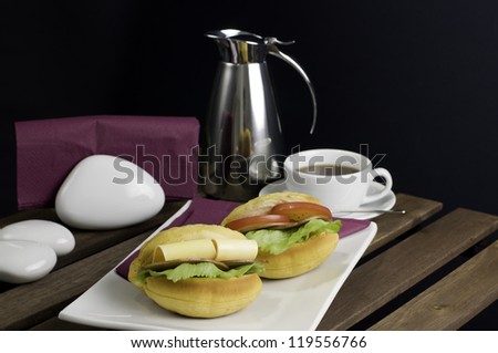 Two sandwich on white china plate, cup of tea and thermos on table
