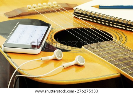 Phone open a note of song with headset notebook and pencil on guitar