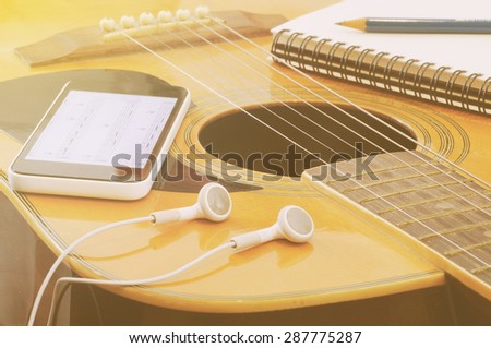 Phone open a note of song with headset notebook and pencil on guitar in vintage tone