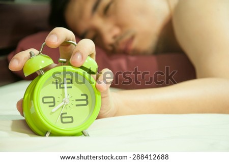 Man lying in bed turning off an alarm clock in the morning at 8am