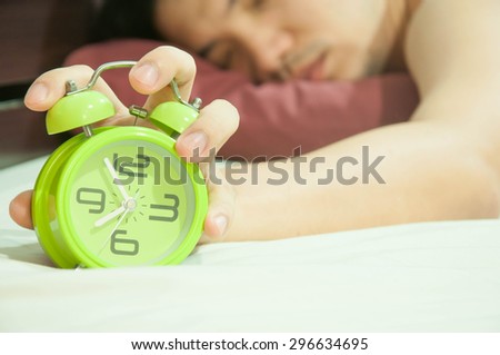 Man lying in bed turning off an alarm clock in the morning at 8am