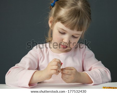 Pretty little girl threading beads and making bracelet
