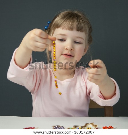 Pretty little girl threading beads and making bracelet, grey background