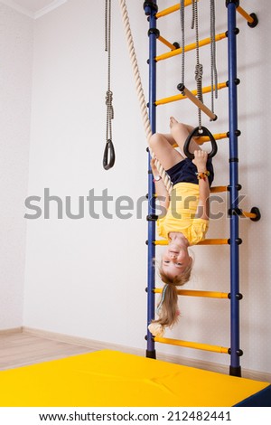 Smiling little girl hanging foremost on a sports ladder
