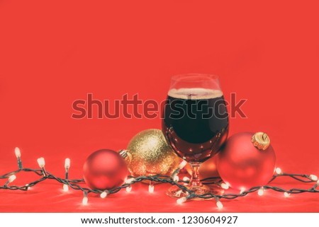 Snifter glass of dark ale or porter beer with  christmas lights and baubles on red background