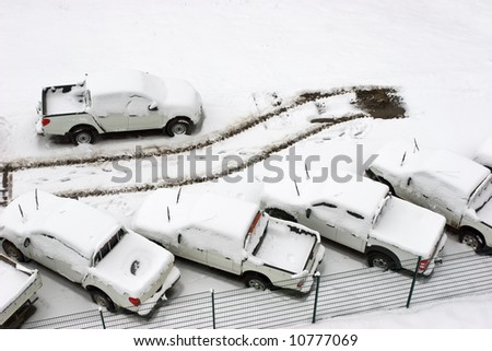 Parked cars under snow at parking lot with tracks of one gone car aerial view