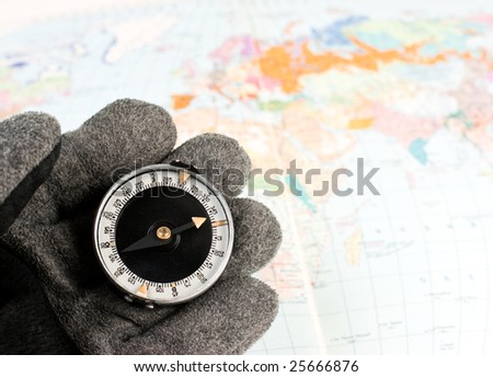 Hand in hiking glove holding compass with map of the world in background