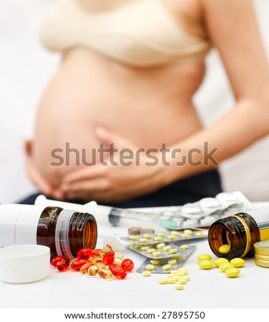 Yellow and red pills spilling from bottles and blisters in front of pregnant woman, shallow DOF