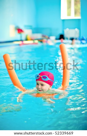 Happy little girl learning to swim with pool noodle
