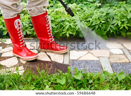 Person in red  gumboots cleaning  garden alley with a pressure washer