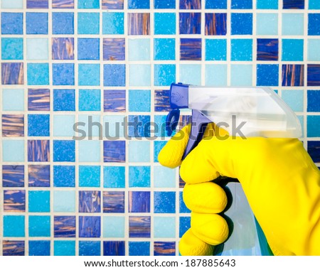 Hand in yellow protective glove holding spray bottle cleaning mosaic wall