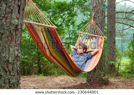 Serene boy lying in striped hammock in summer forest