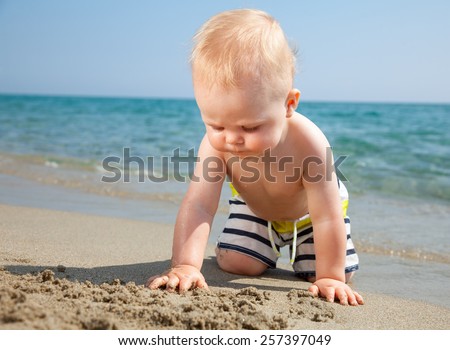 10 month baby boy wearing swimming shorts playing on a beach