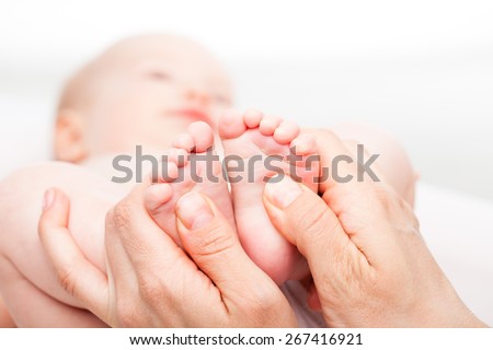 Close-up shot of three month baby girl receiving foot massage from a female massage therapist. Camera is focused on infant\'s feet. Face is blurred in background.
