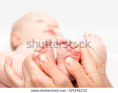 Close-up shot of three month baby girl receiving foot massage from a female massage therapist. Camera is focused on infant\'s feet. Face is blurred in background.