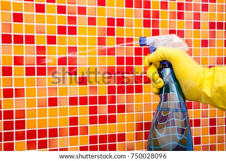 Person doing chores in bathroom at home cleaning red orange tiled wall with spray detergent