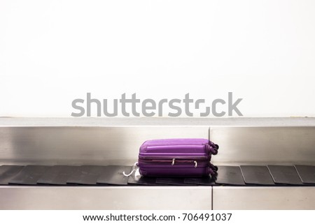A purple luggage is laying down on the conveyor belt at the airport. Baggage claim. White wall background.