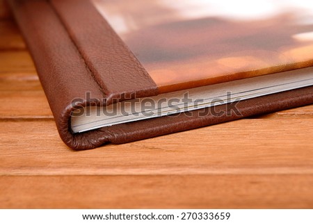 Big photobook lay on wooden table close up. Hard leazard cover