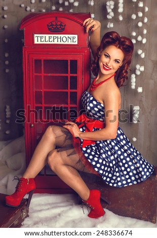 Pretty vintage pin-up girl near red english telephone booth