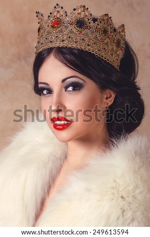 Fashion portrait of a sexy brunette model in golden vintage queen crown and white fur coat