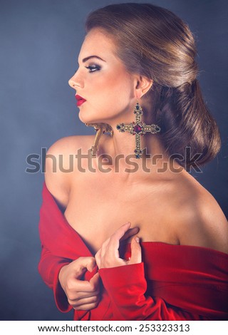 Beautiful retro woman vintage posing with naked shoulders in red dress with crosses earrings on black background