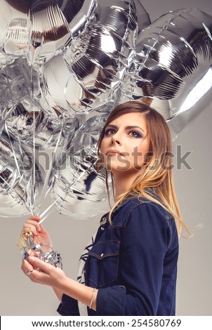 Beautiful cool thoughtful teen girl in blue jeans shirt with ombre hair with silver balloons in her hands