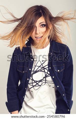 Cool smart teenager girl in jeans shirt with funny curious face and blowing hair