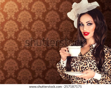 Beautiful retro brunette smiling woman portrait in leopard blouse with red plump lips in vintage veil hat with white cup in her hands on blur brown pattern background with copy space