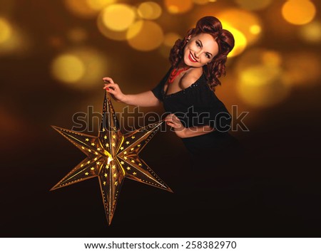 Beautiful vintage pin-up girl holding shining lightning metal star in her hands on dark background with copy space