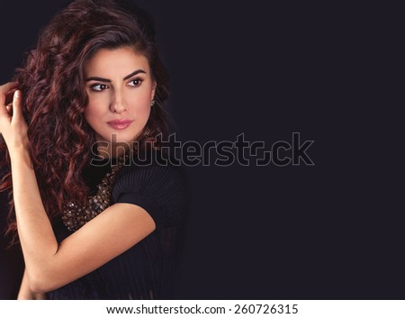 Beautiful young latin woman face, holding her long wavy hair, looking to the left and thinking on a black background with empty copy space