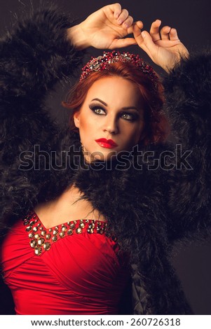 Sexy red hair woman with party make up in red dress with golden crystals and black fur coat raising her hands up