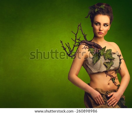 Beautiful woman in decorative costume of ecology nature forest tree with leaves on green background with copy space. Save eco planet concept