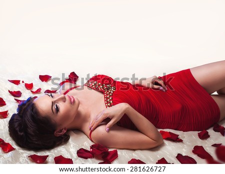 Sexy beautiful brunette woman in red dress laying on a bed with romantic rose petals