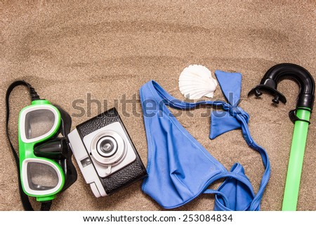 Old camera, bikini and shell on sand