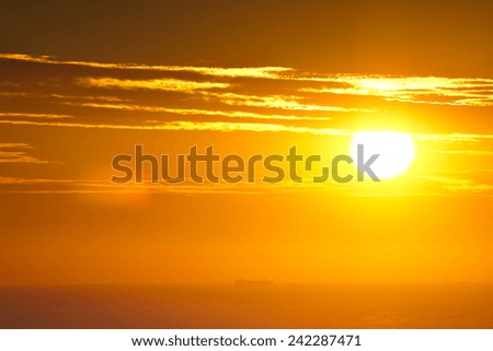 The sun rises over the ocean as a ship sails past on the horizon.