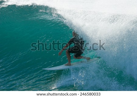 A surfer guides himself and his surfboard through a beautiful blue tube on an ocean wave.