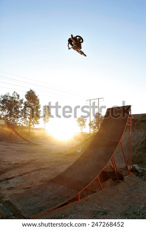 A freestyle motocross rider flies through the air above a ramp on his motorbike as the sun sets.