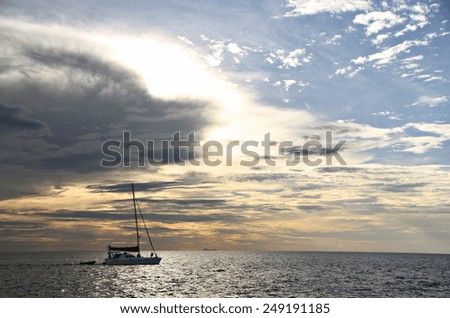 A yacht cruises along as the sun sinks towards the horizon.