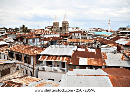 A view across the rusted corrugated iron roofs of Stone Town in Zanzibar, Tanzania, showing the steeples of a Christian church and the minaret of a Muslim Mosque.