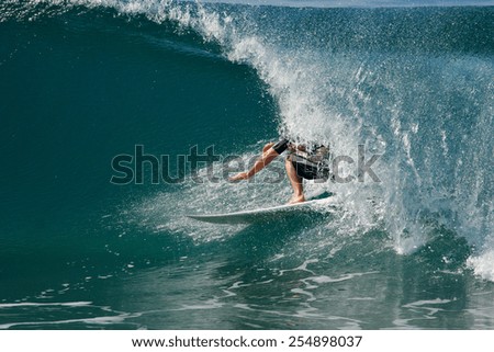 A surfer rides a tube on a beautiful, blue wave in the ocean.