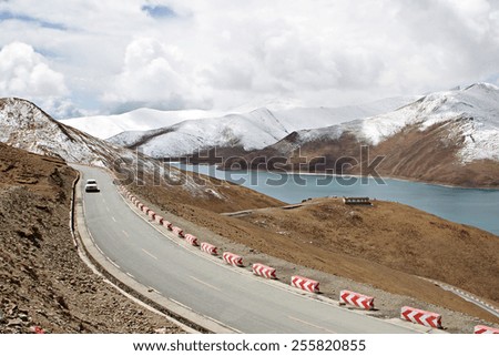A car drives along the Friendship Highway past Yamdrok Lake in rural Tibet.