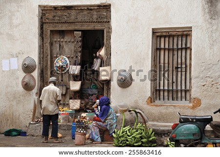 A man trades with a women on the street outside of her tiny shop in Stone Town, Zanzibar, Tanzania.