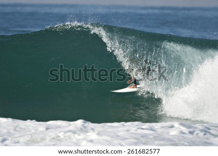 A surfer rides a tube on a beautiful blue wave.